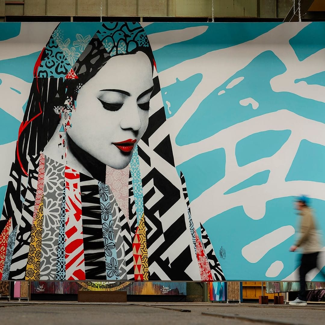 Ce graffiti représente une femme avec un voile sur la tête plein de couleurs et de motifs avec un fond bleu.