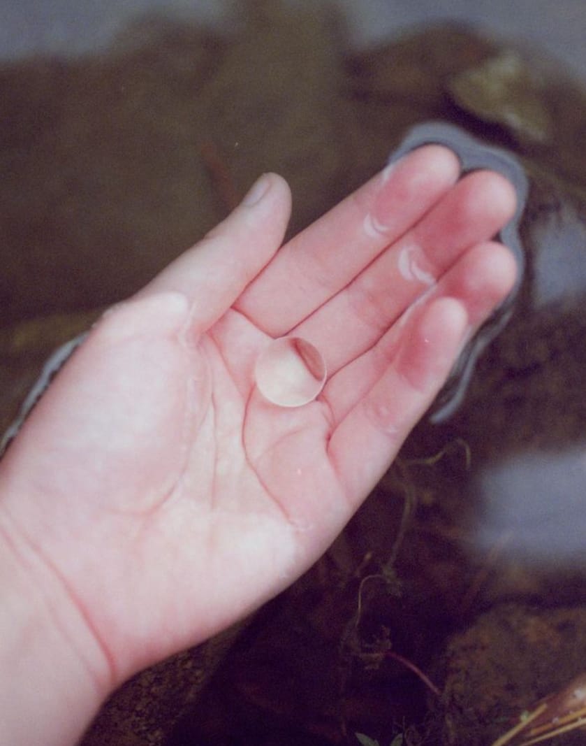 Photographie d'une main à la surface de l'eau avec une bille transparente dans son creux par Li Hui